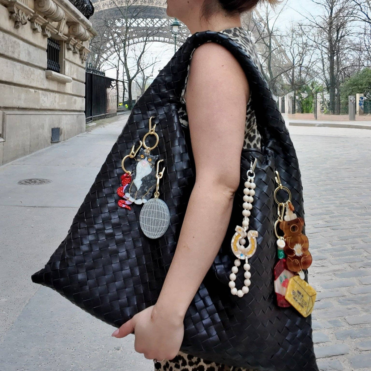 Woman with a large black handbag featuring various accessories in front of the Eiffel Tower.