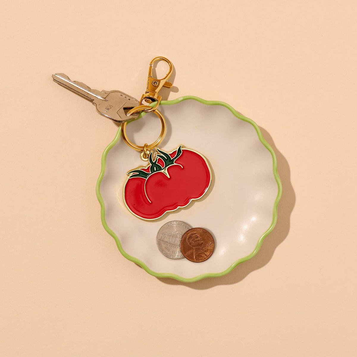 Keychain with tomato design on a shell-shaped dish with coins on a beige background