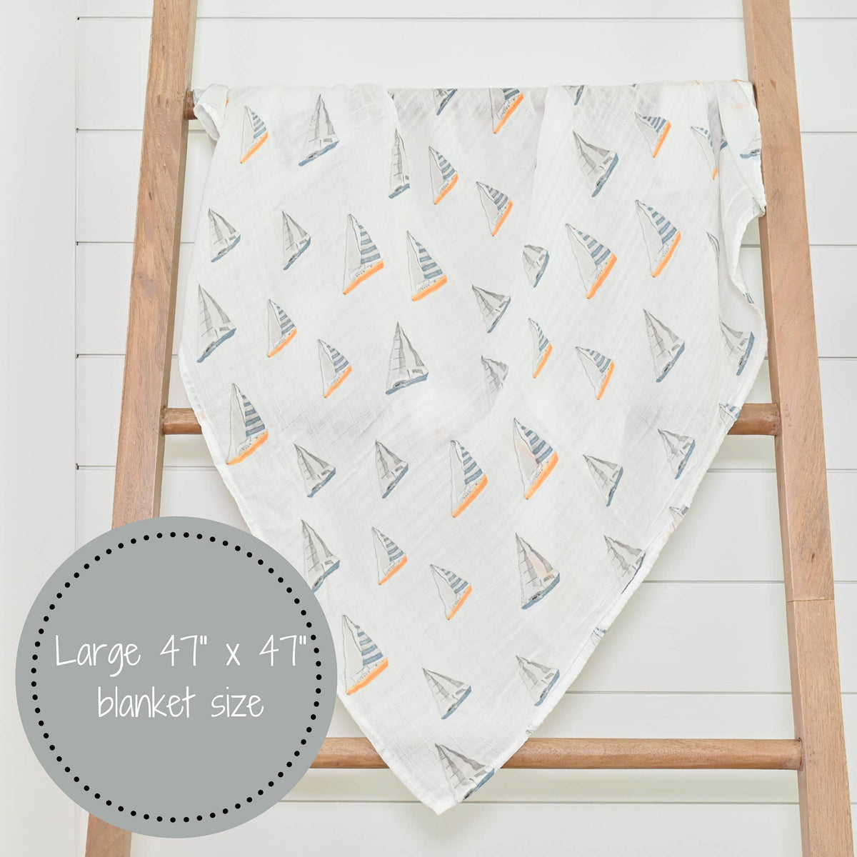 Blanket with sailboat pattern draped over a wooden ladder on a white background