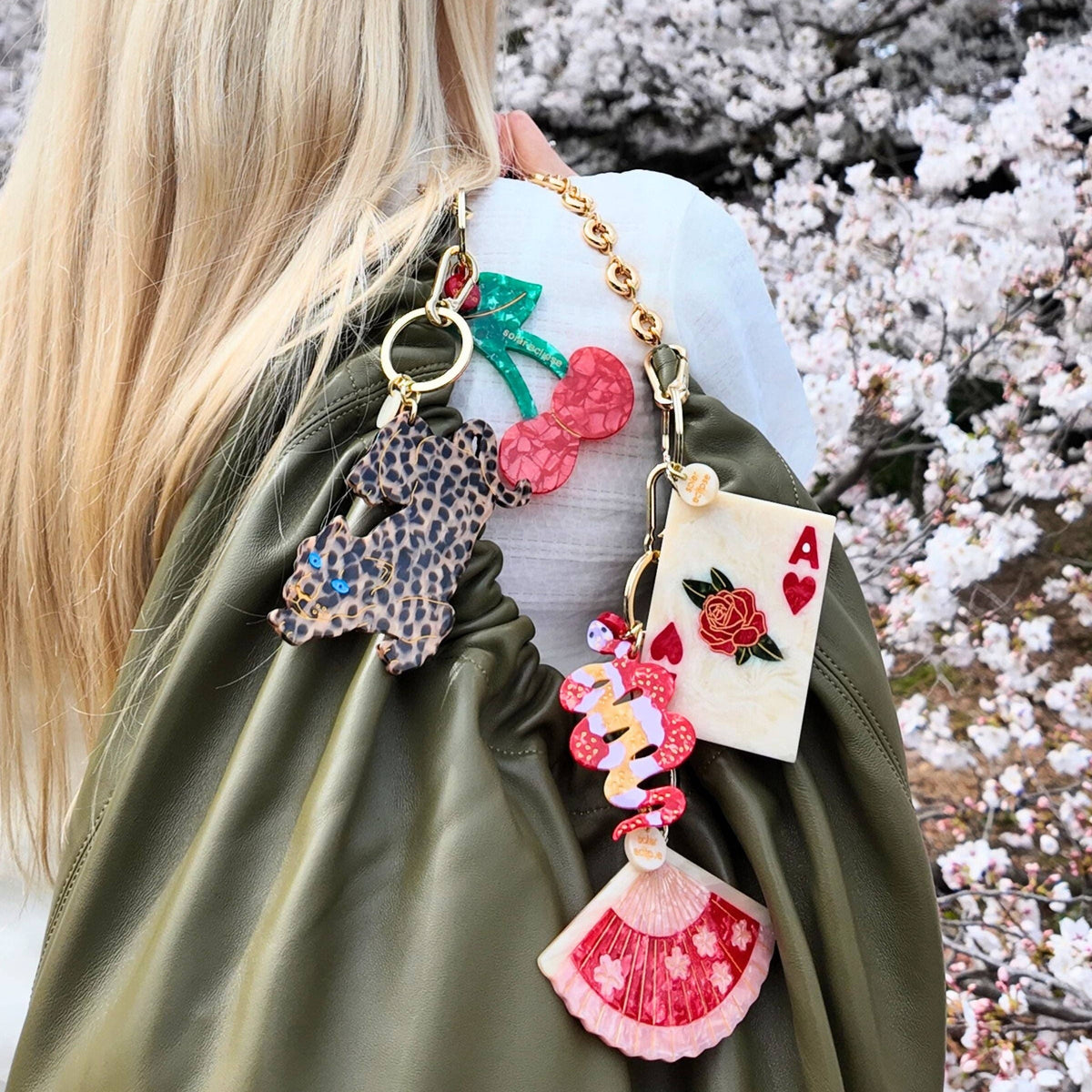 Person wearing a green bag with a colorful handbag featuring various charms against a cherry blossom background.