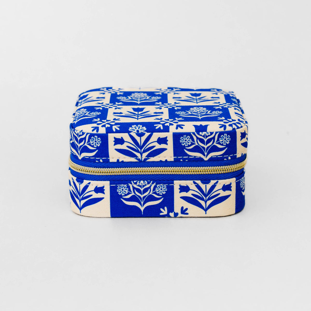A square zippered case with a blue and cream floral block print pattern, featuring a gold zipper, set against a plain light gray background.