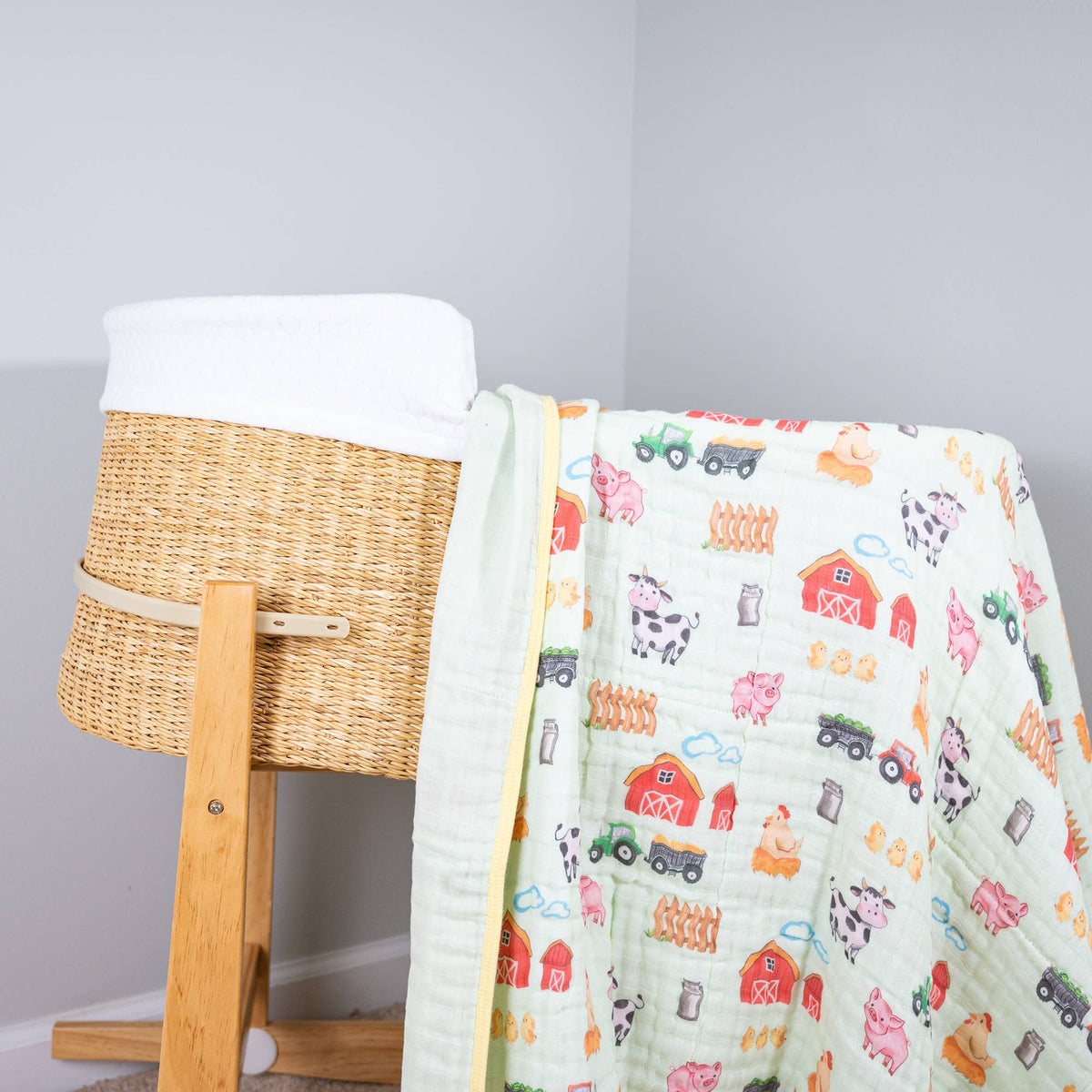 Children's quilt with farm-themed design draped over a wicker basket on a light gray background
