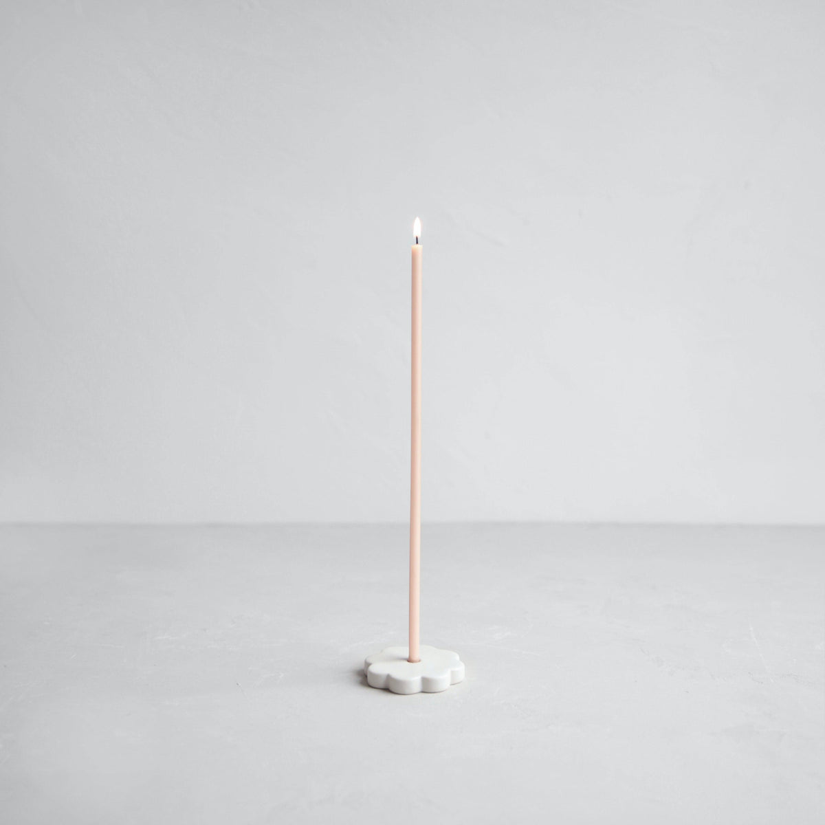 Tall candle on a white base against a light gray background