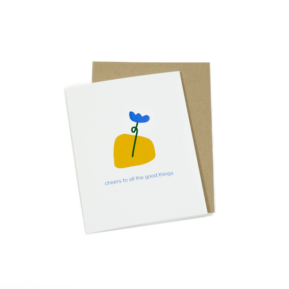 A white greeting card with a minimalist illustration of a yellow shape, a blue flower, and the text 'cheers to all the good things', shown with a brown kraft envelope on a white background.