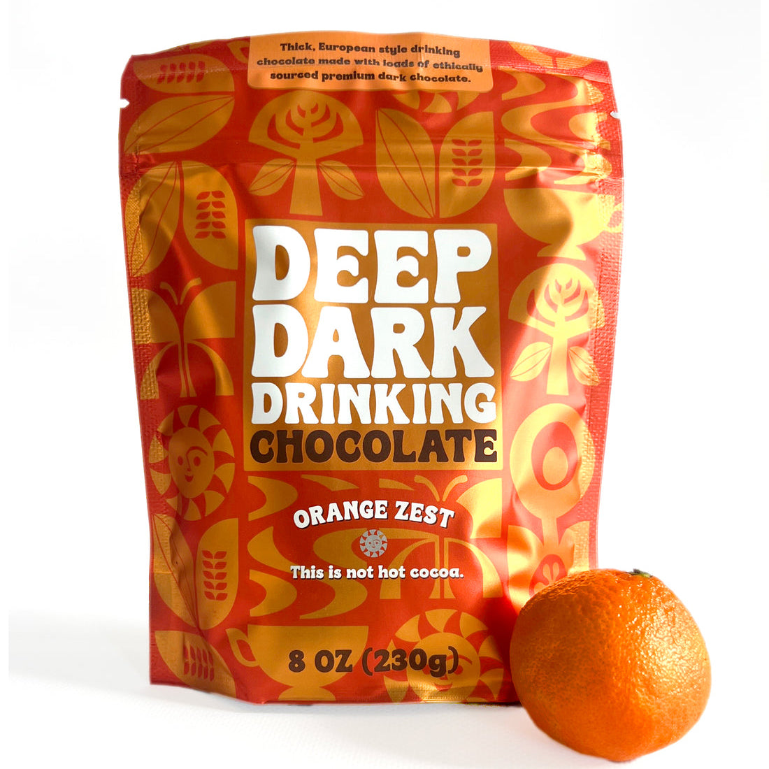 A package of Deep Dark Drinking Chocolate in Orange Zest flavor, featuring bright orange patterned packaging with bold white lettering, pictured alongside a whole orange on a white background.