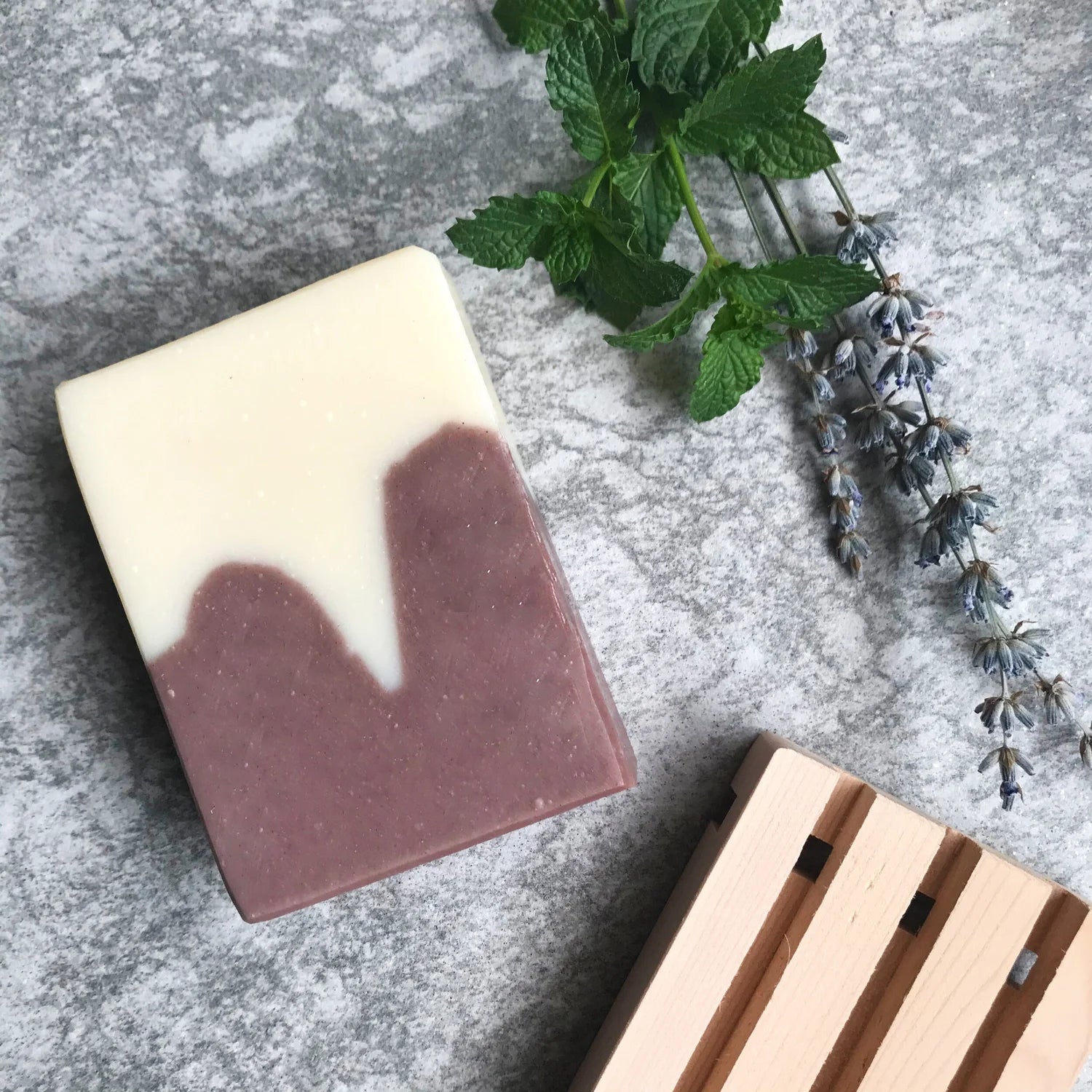 Two-toned soap bar with a wooden soap dish and lavender on a gray surface