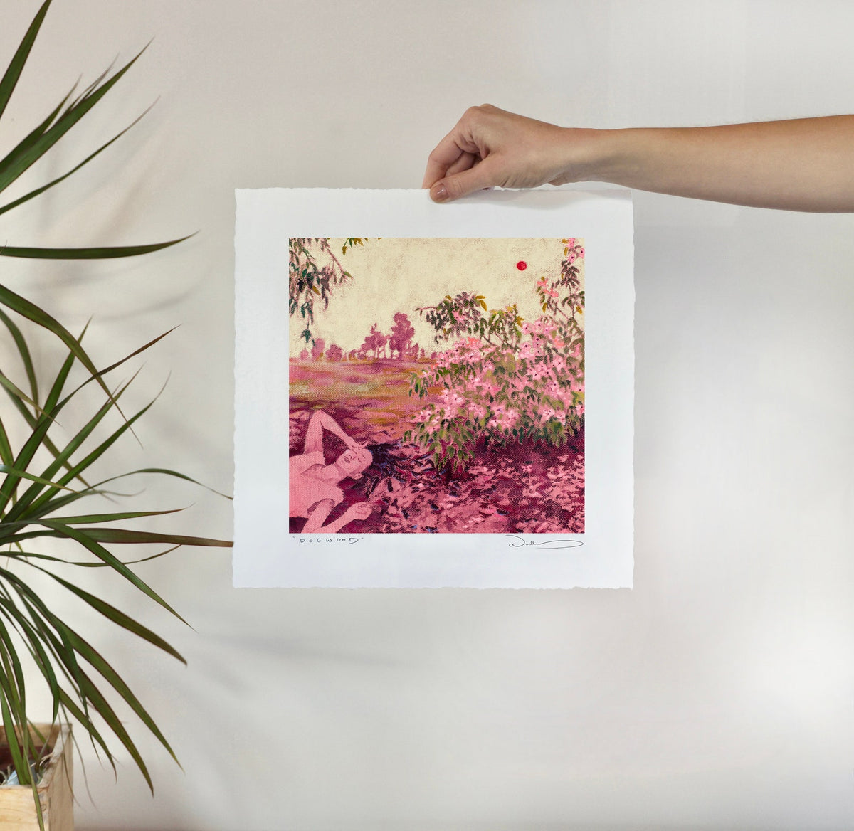 print held against a white wall with plants.
