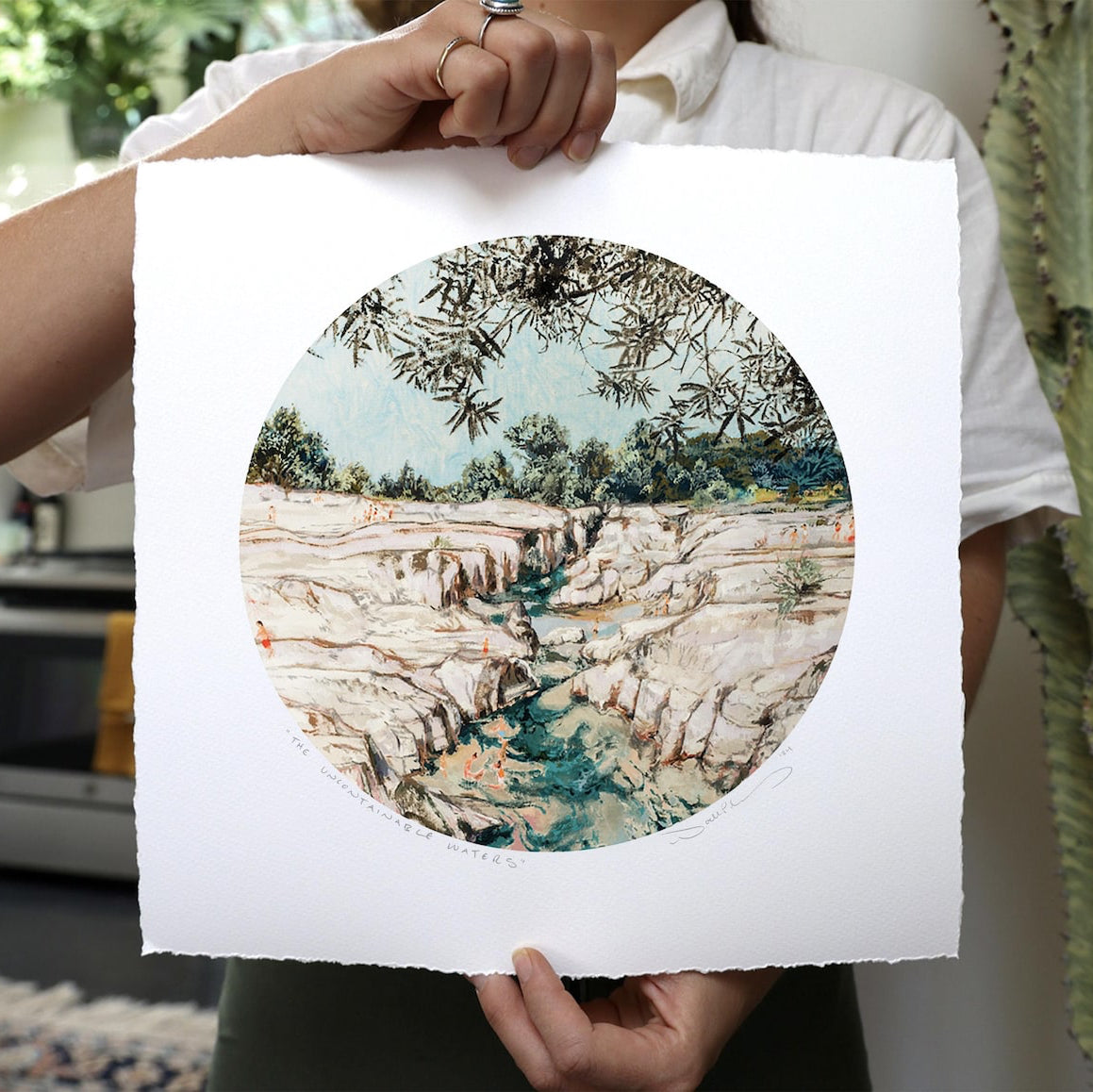 Sandy rocks with sprigs of tree branches surround a current of water with people.