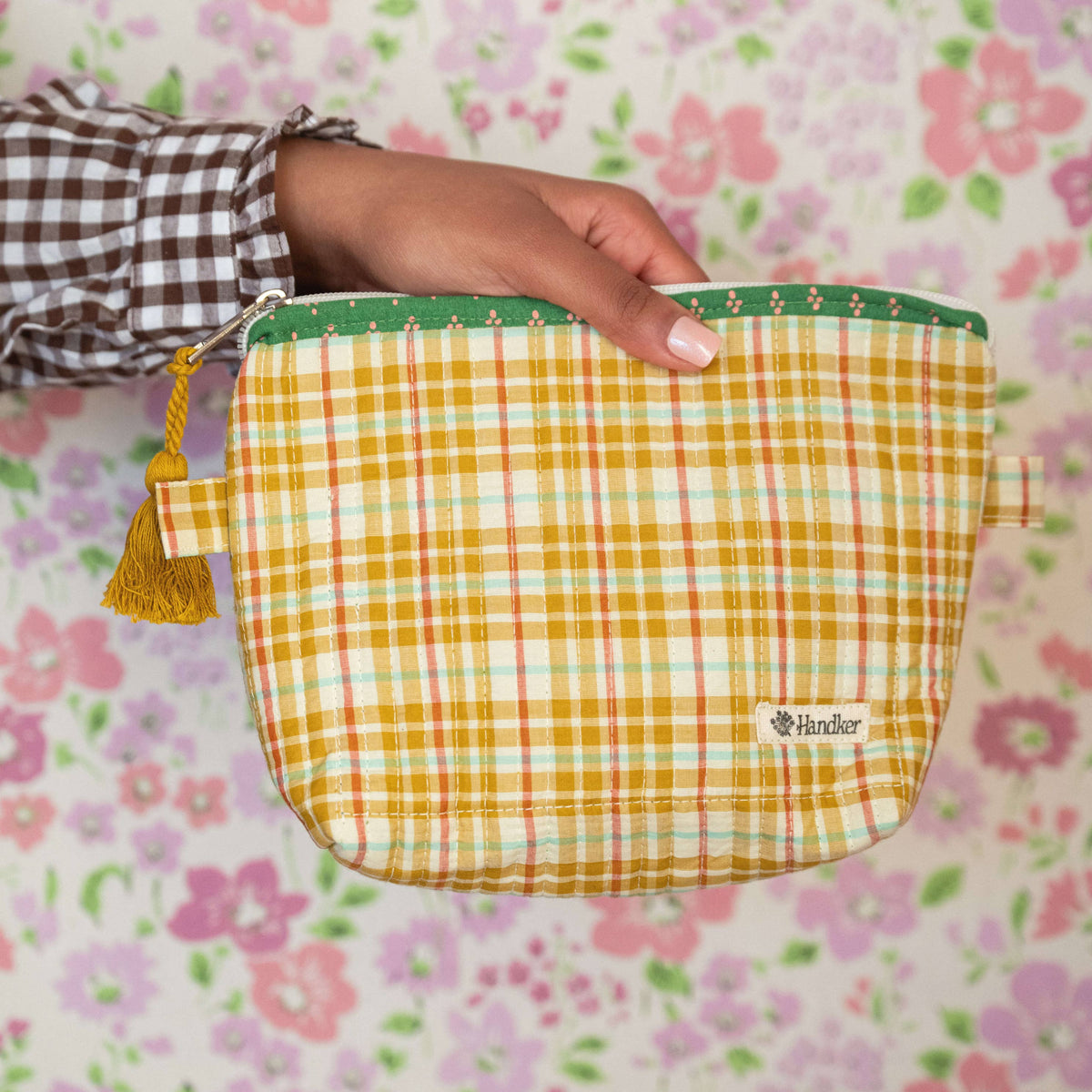 Person holding a yellow checkered pouch with a floral patterned background