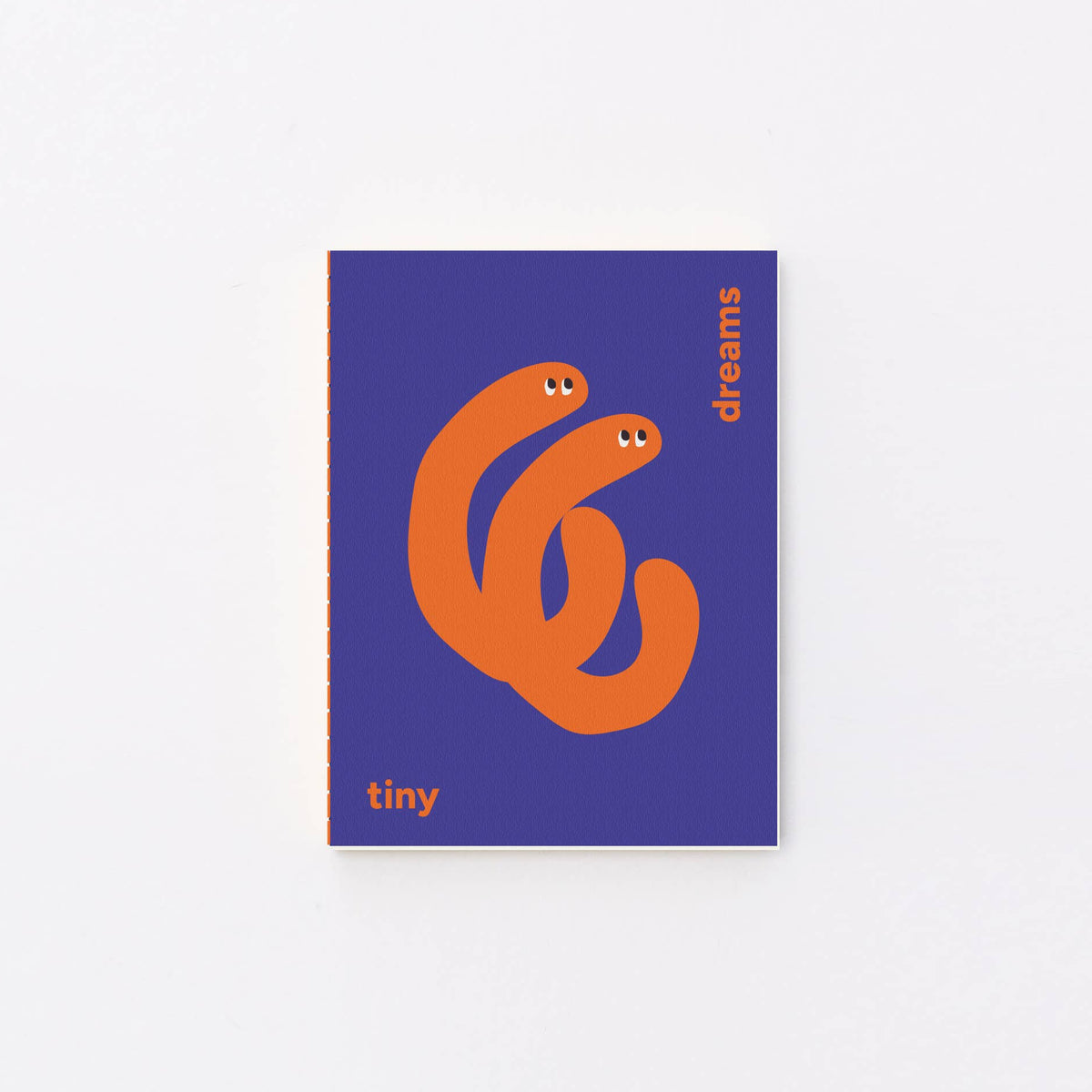 A small notebook or book cover centered on a light gray background. The cover is purple with an orange abstract snake-like graphic and small orange text reading 'tiny' and 'dreams'.