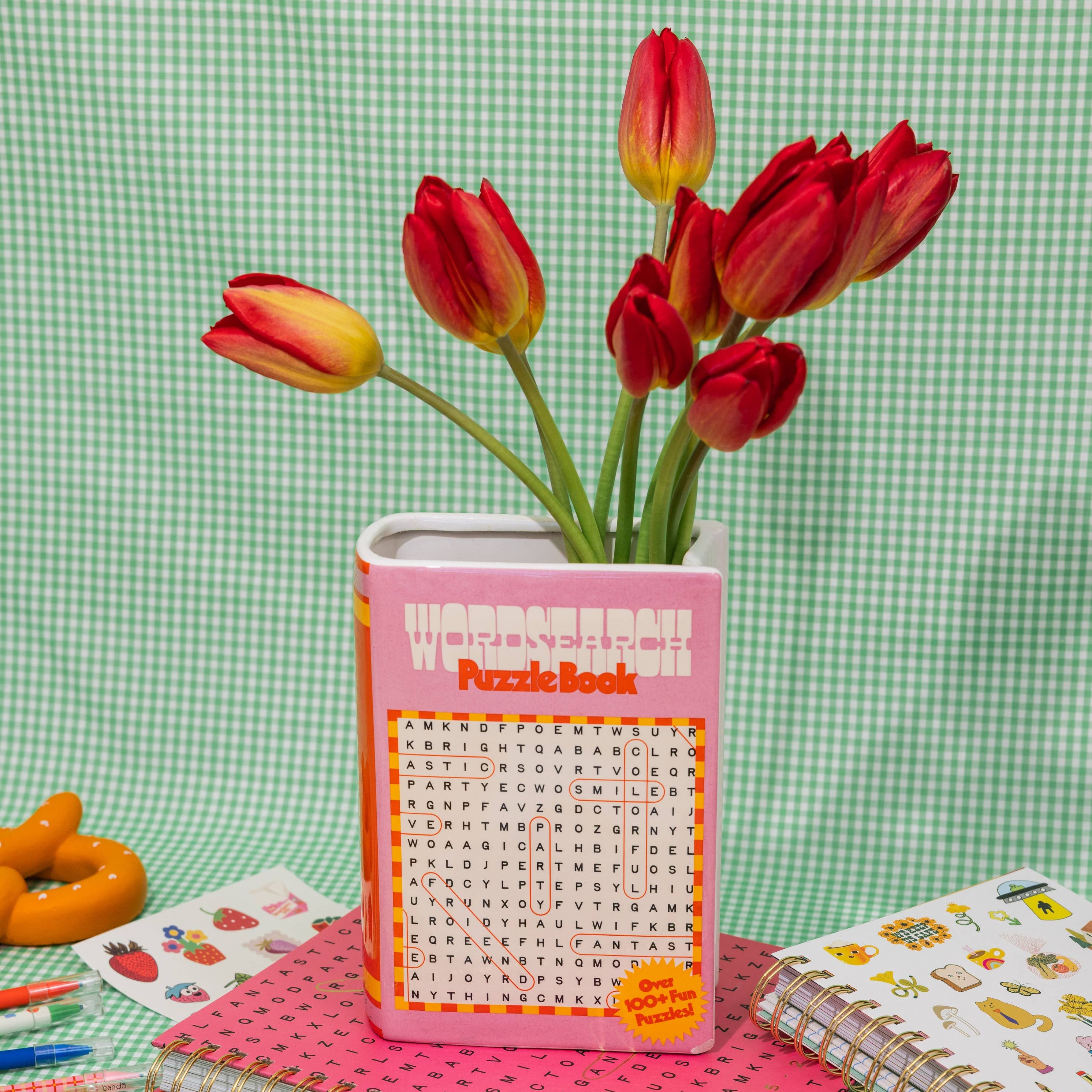 Pink puzzle book vase with red tulips on a green checkered background