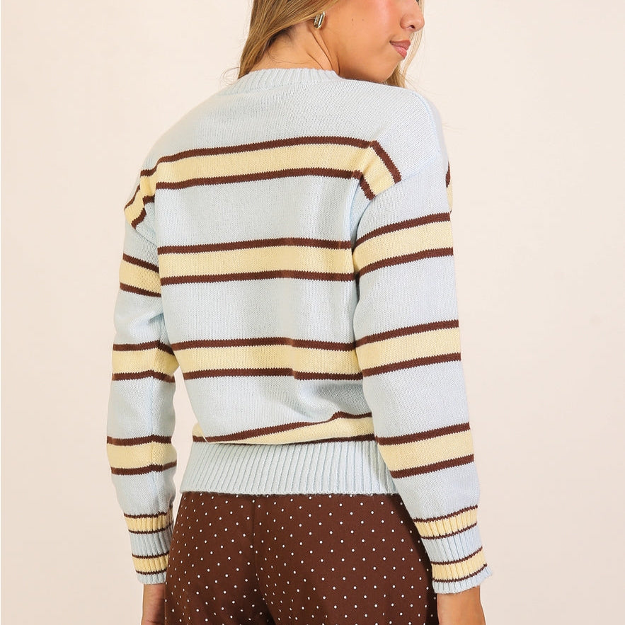 Woman wears a light blue crewneck sweater with horizontal yellow and brown stripes. 