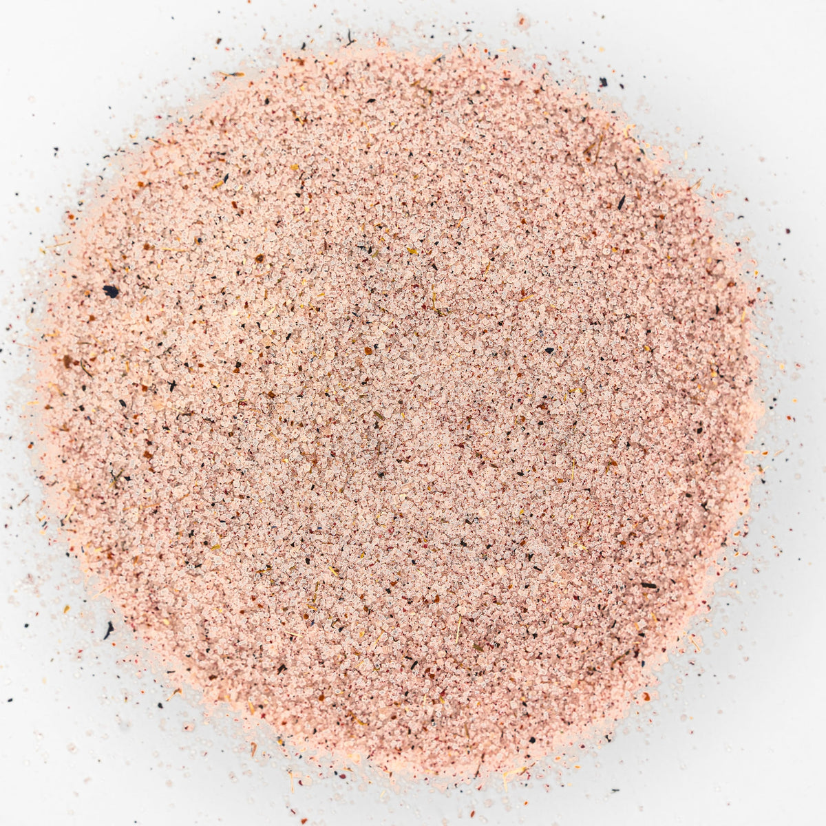 Pile of light pink salt with flecks of blue herbs. 