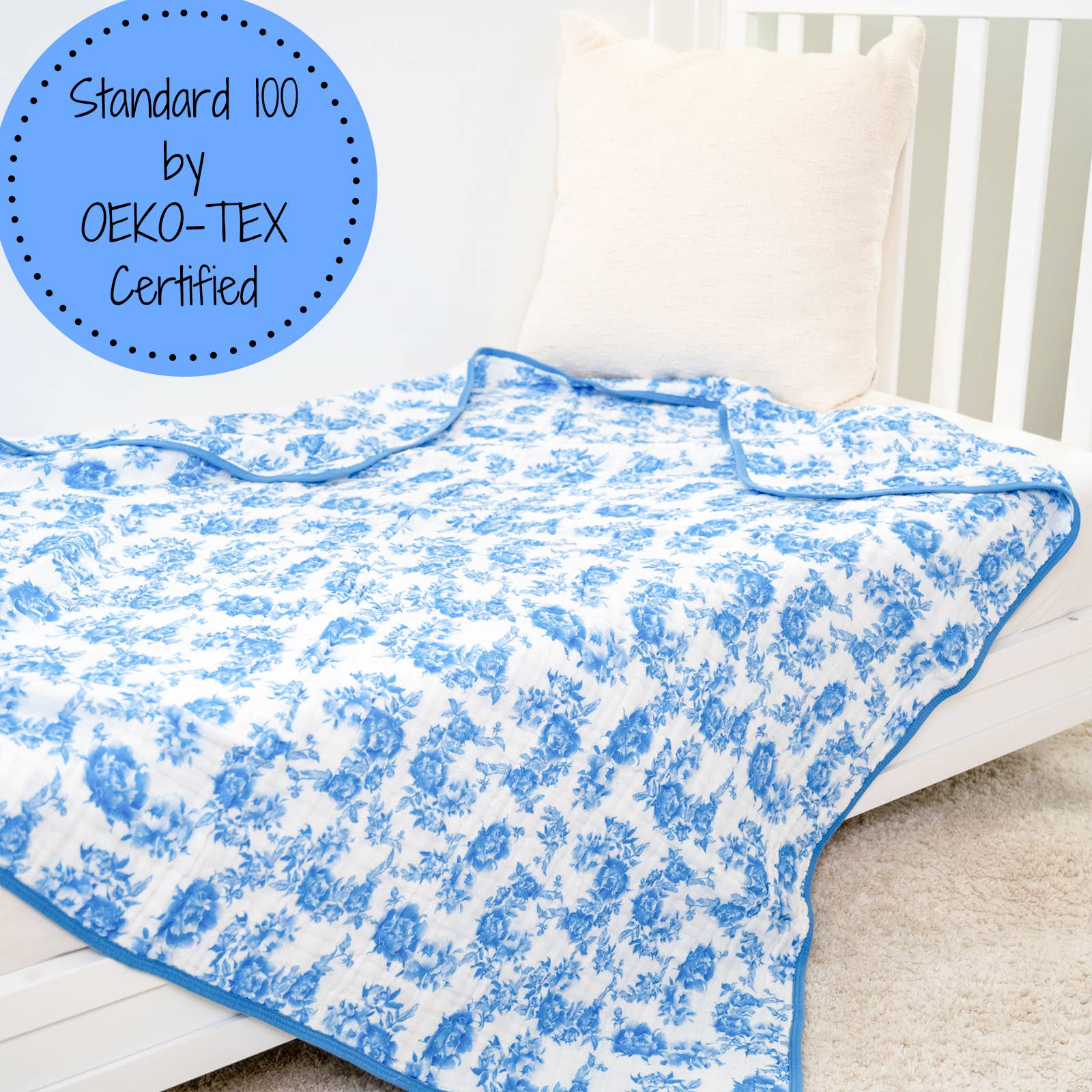 Blue floral patterned blanket on a white bed with OEKO-TEX certification label.