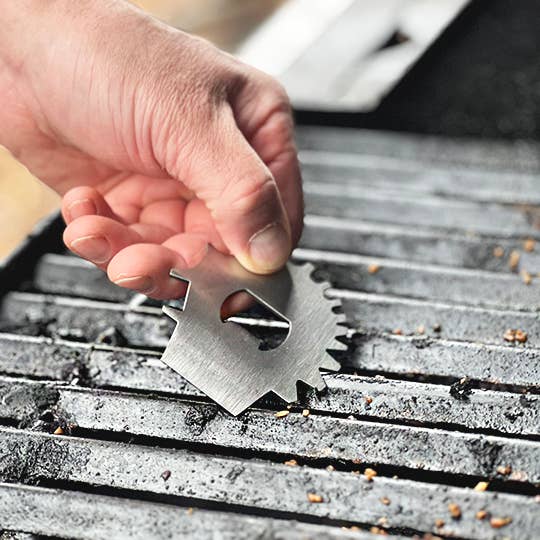 Hand using a metal grill cleaning tool on a grill grate