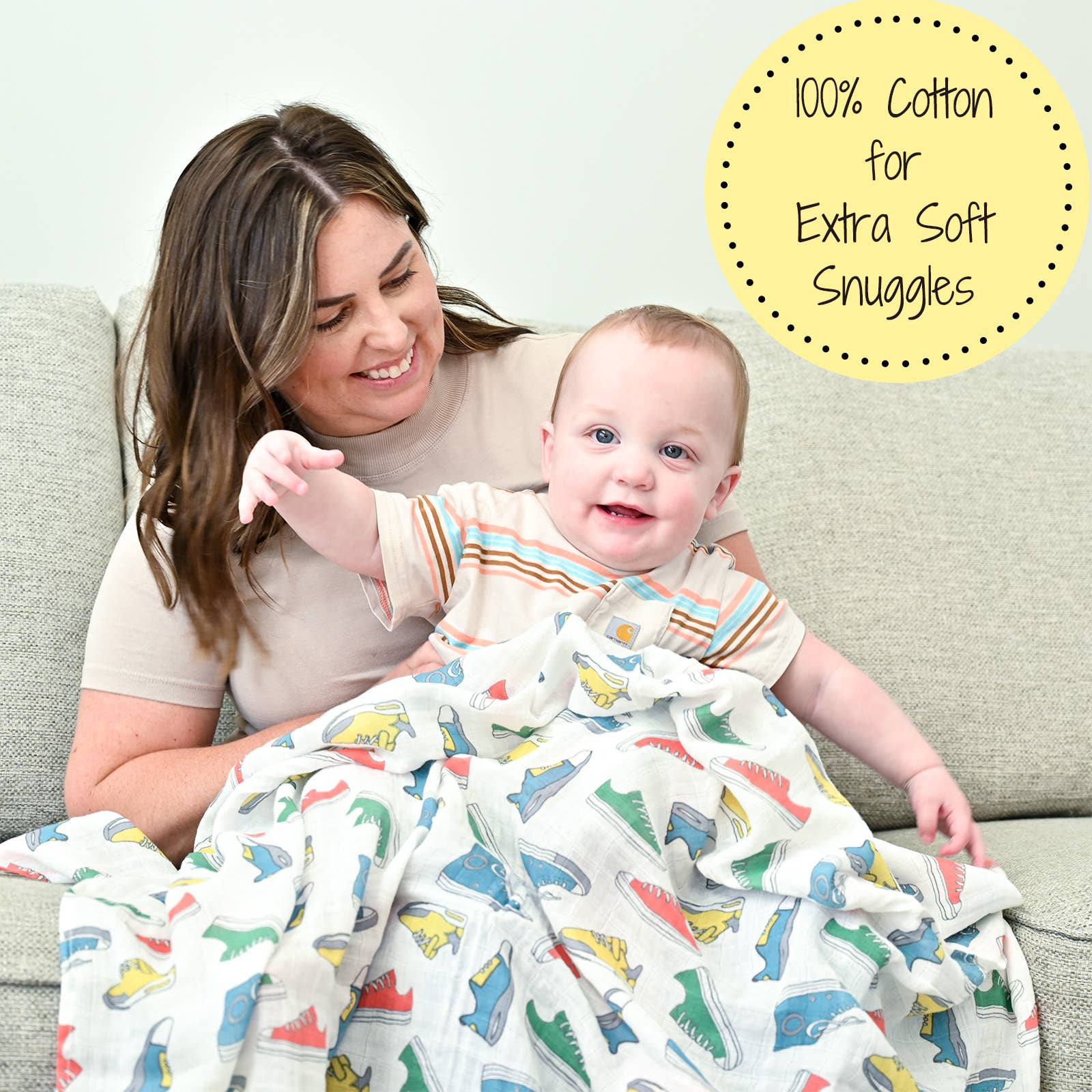 Woman holding a baby wrapped in a dinosaur-patterned blanket with text about 100% cotton.