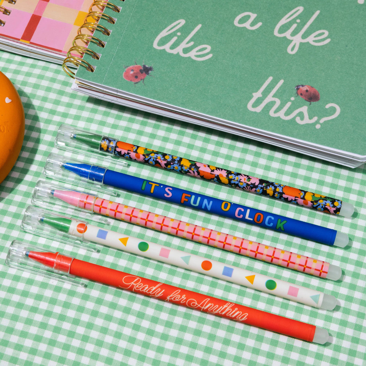 Colorful pens and a green notebook with text on a checkered tablecloth