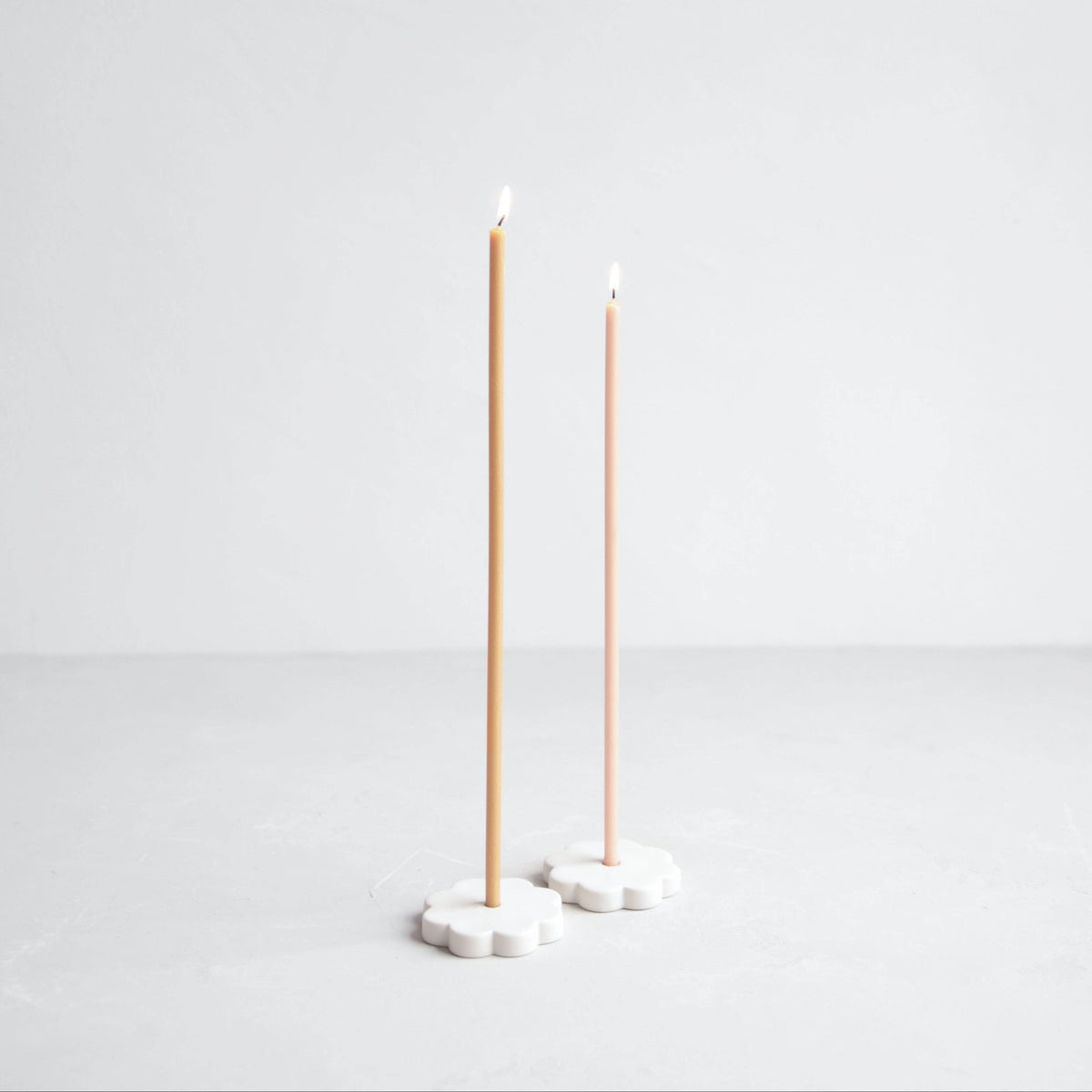 Two tall, thin candles on white stands against a light gray background