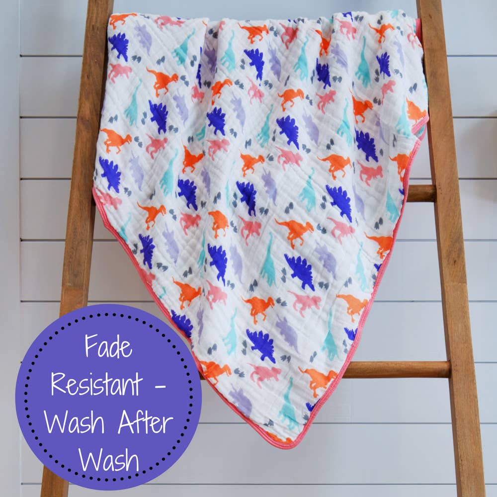 Baby blanket with colorful dinosaur pattern draped over a wooden ladder on a white wooden floor.