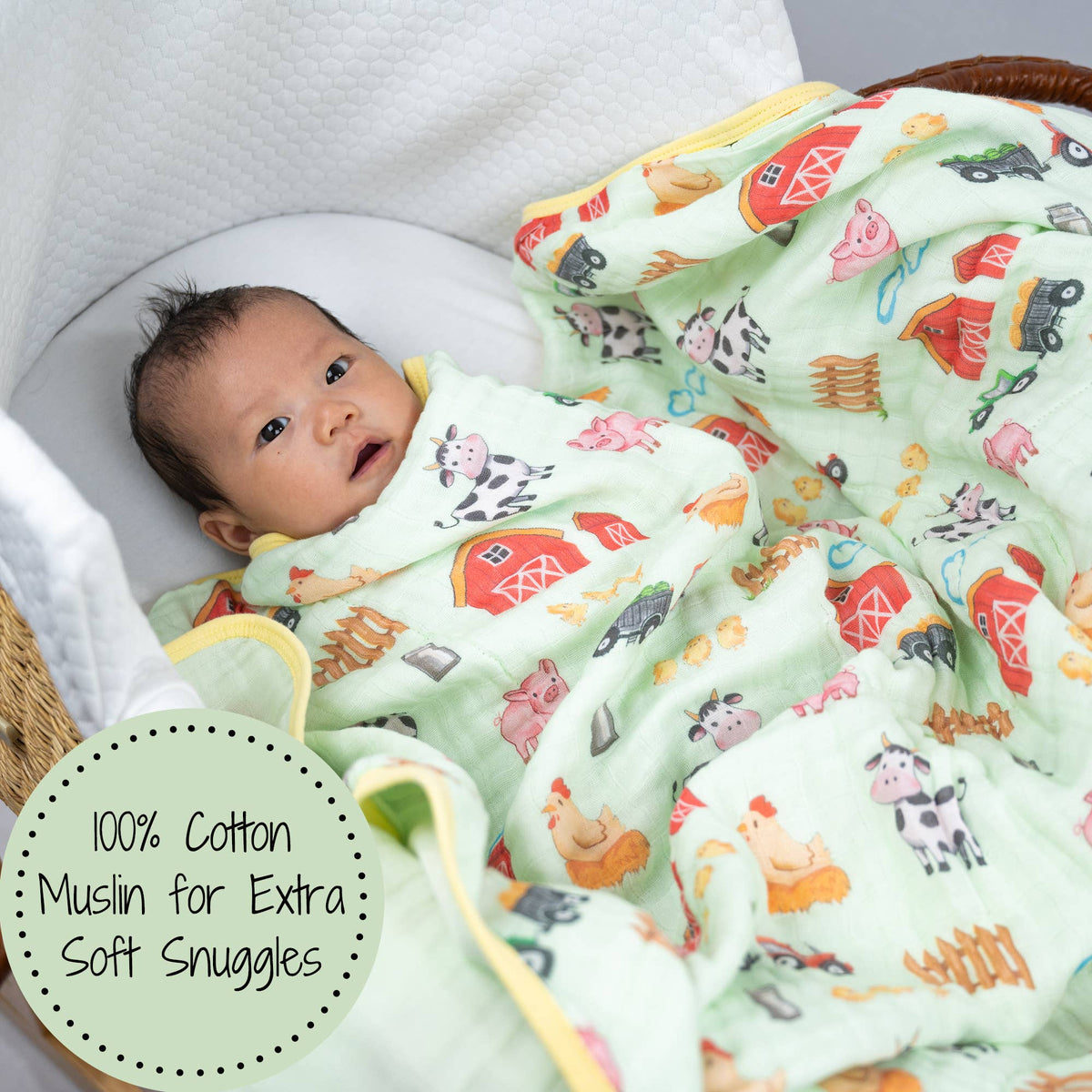 Baby wrapped in a colorful farm-themed blanket with a label indicating 100% cotton muslin.