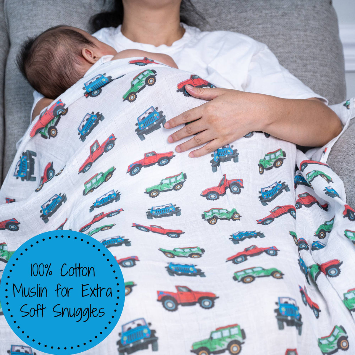 Baby wrapped in a white muslin blanket with colorful car patterns, held by an adult.