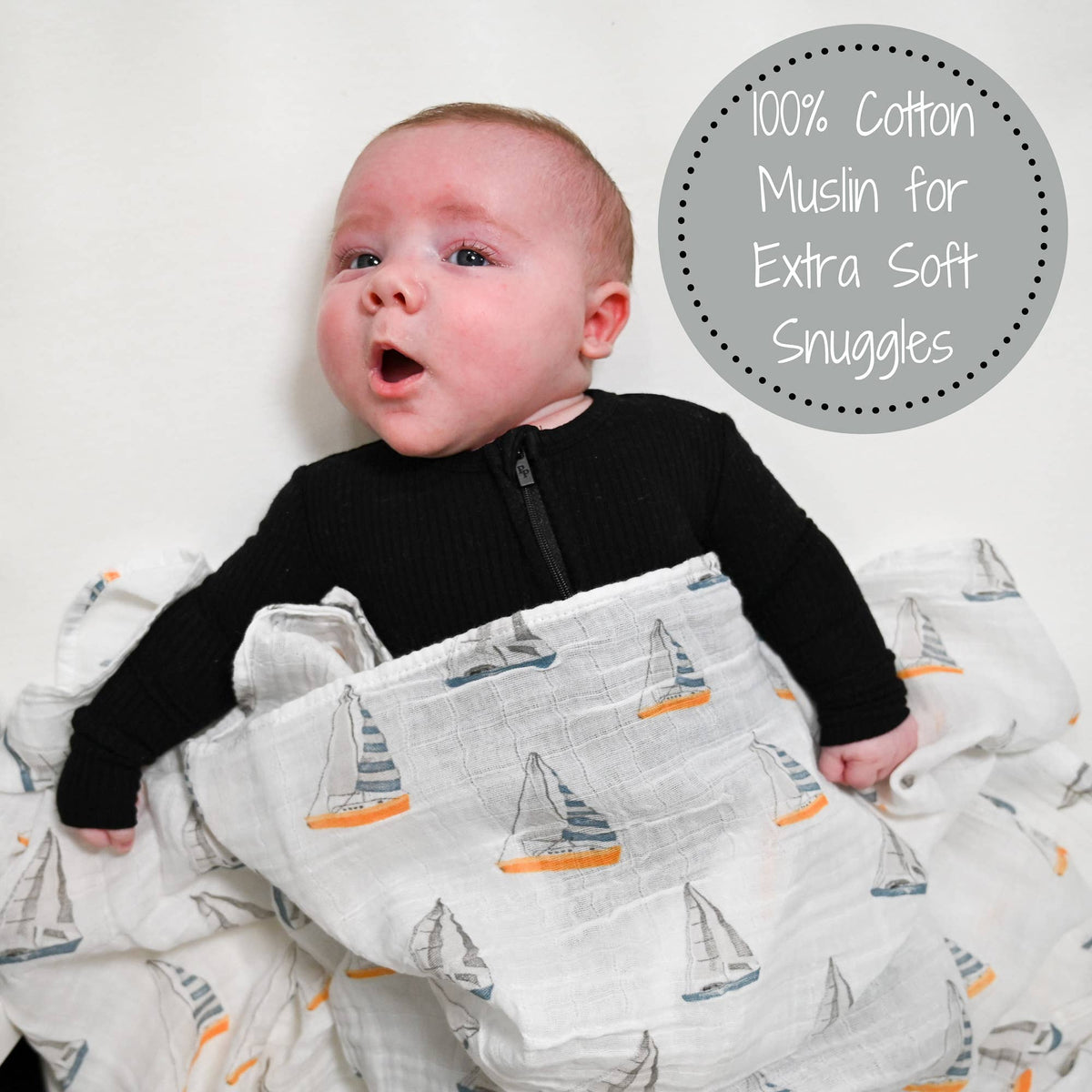 Baby wrapped in a 100% cotton muslin blanket with sailboat pattern, on a white background.