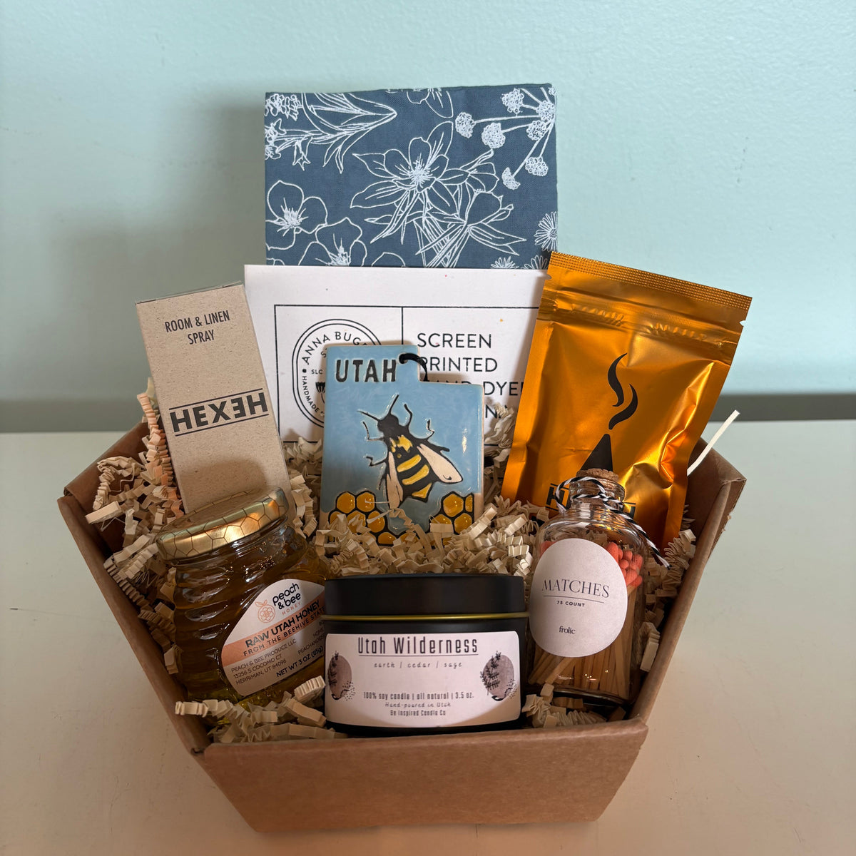 Gift box with various items including a jar, cards, and a bottle on a light blue surface.