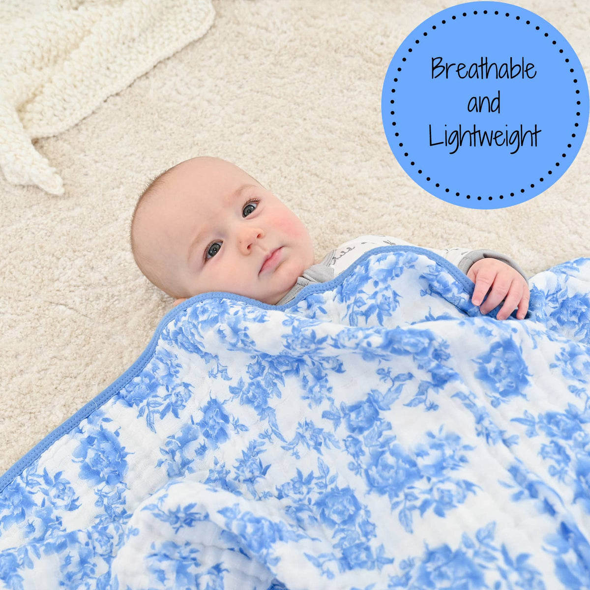 Baby lying on a blue floral blanket with a label 'Breathable and Lightweight' on a beige carpet.