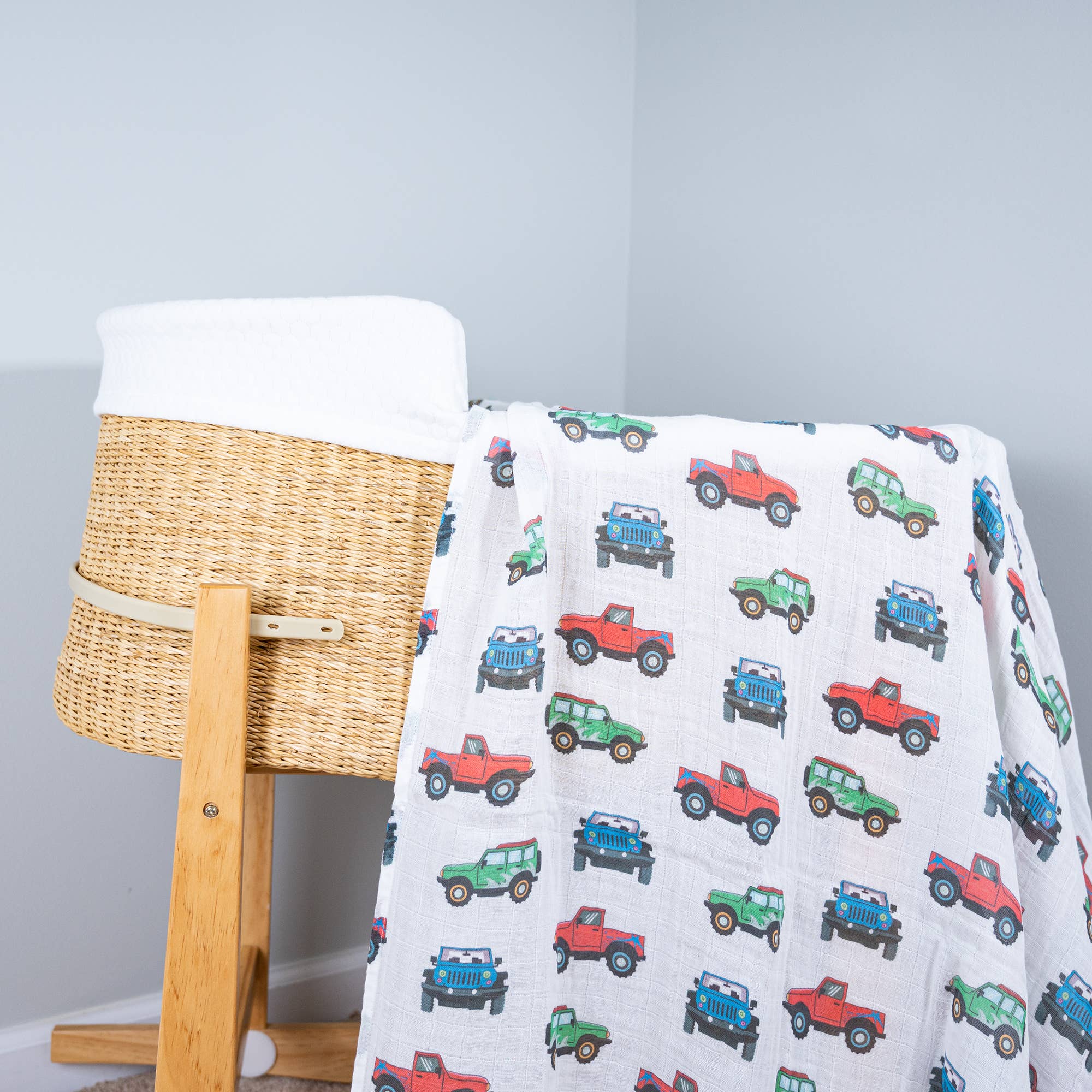 Baby blanket with toy car pattern draped over a wicker basket on a light gray background