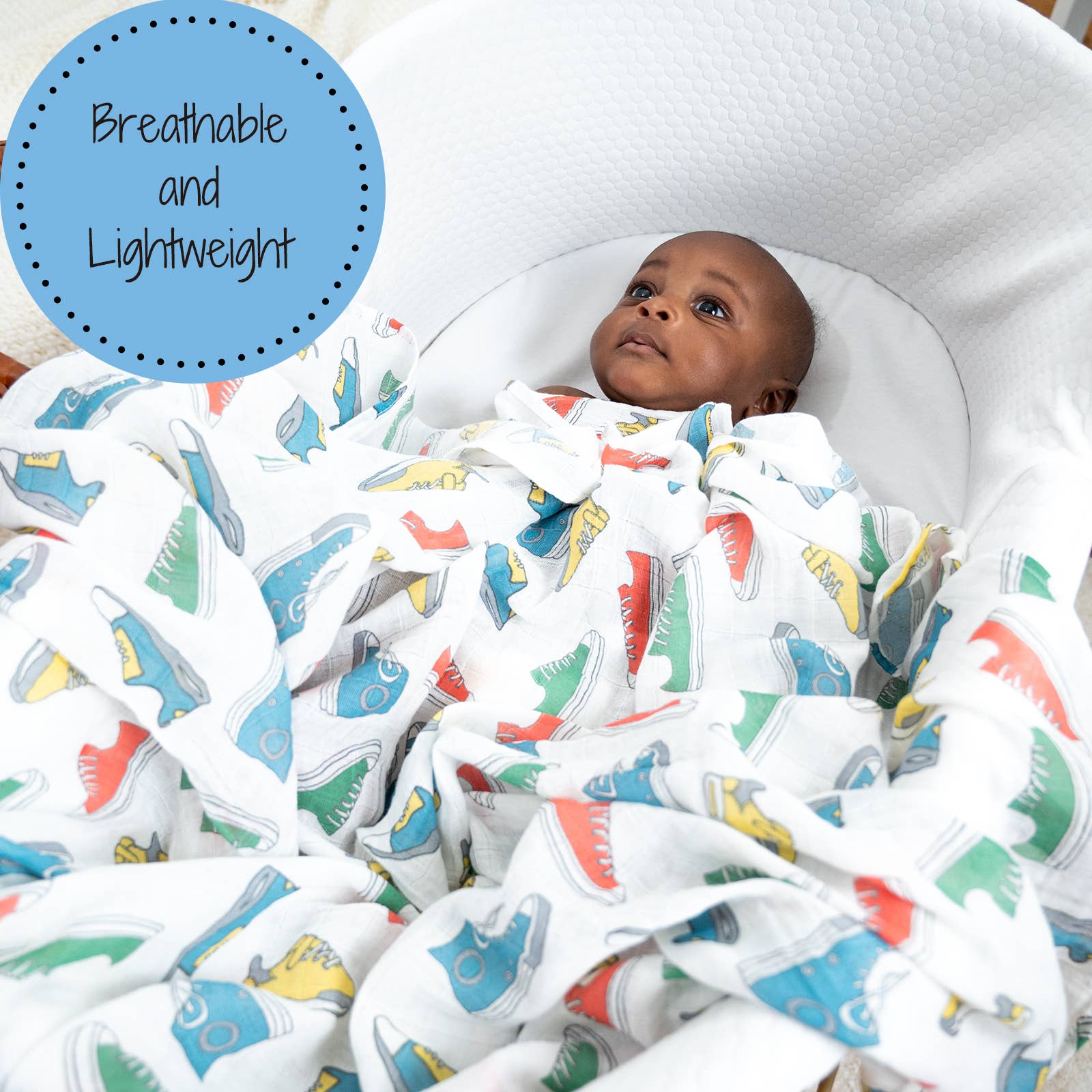 Baby wrapped in a colorful blanket with shoe pattern, lying on a white surface.