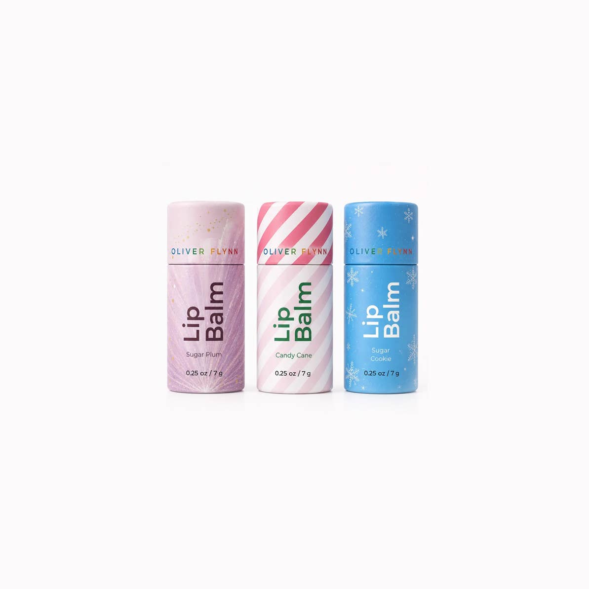 Three Oliver Flynn Lip Balm tubes lined up on a white background: a pink Sugar Elm tube, a white and pink striped Candy Care tube, and a blue Snowflake tube.