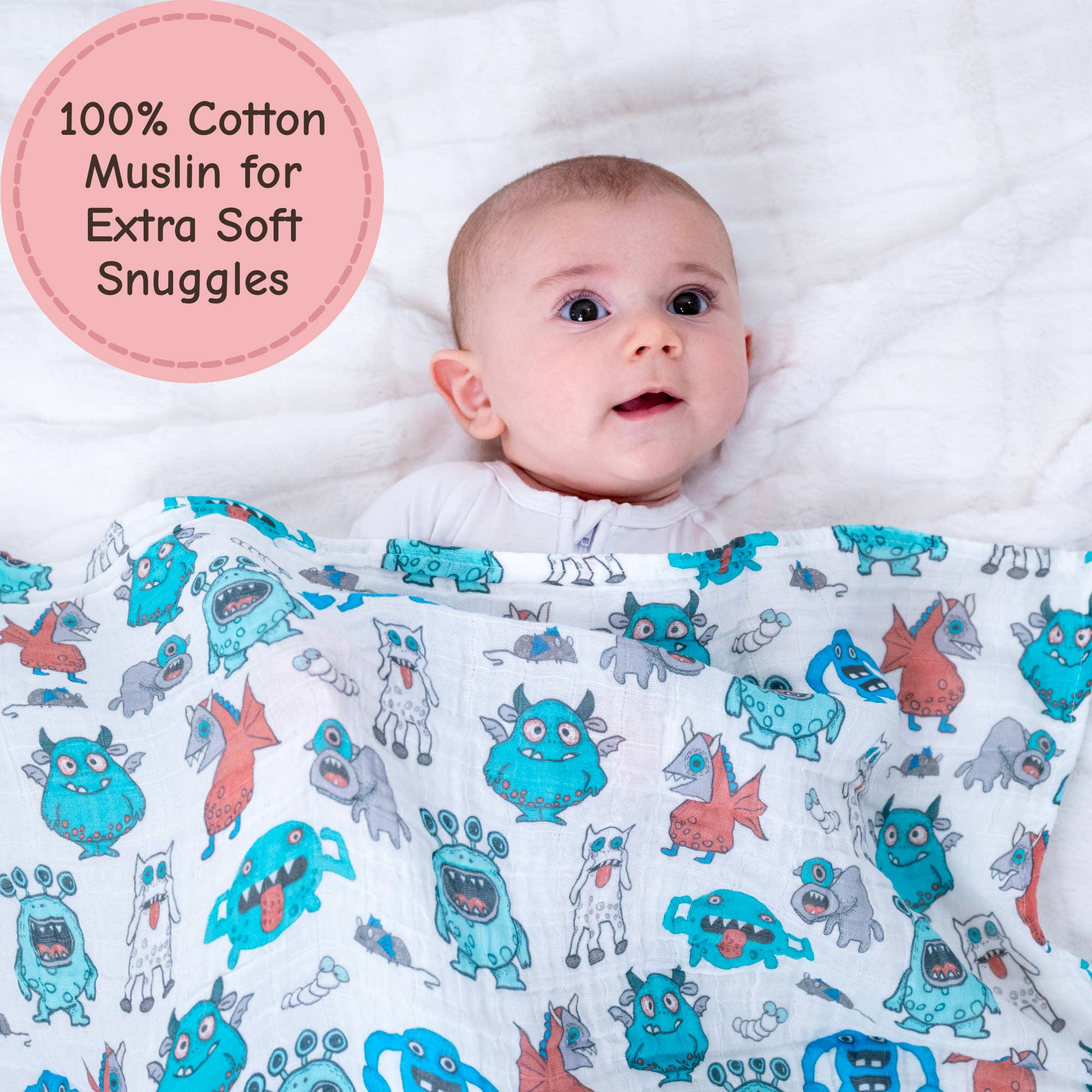 Baby wrapped in a colorful monster-patterned blanket with a pink label indicating 100% cotton.