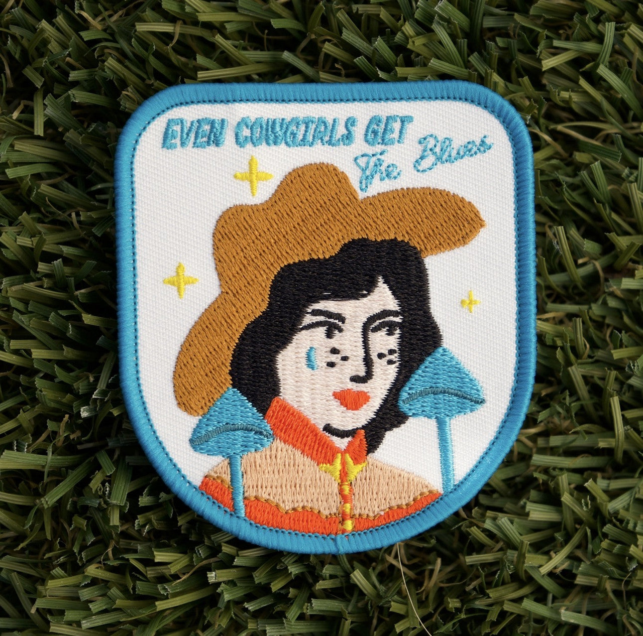 Iron-on embroidered patch with a blue border and white background, a cowgirl with the words "Even cowgirls get the blues".