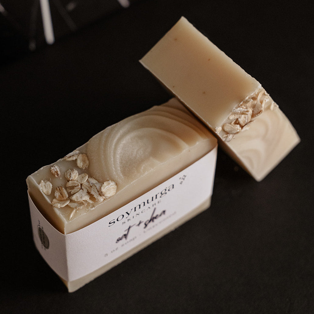 Oat + Shea bar of soap on a black countertop with black marble subway tile in the background. 