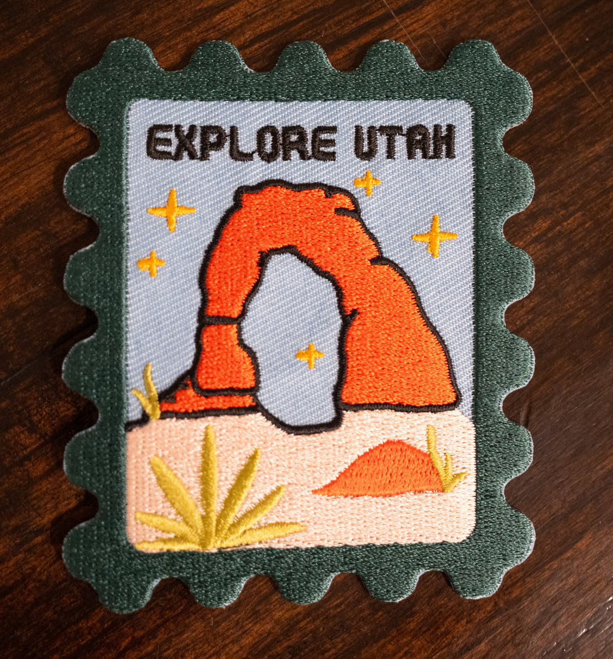 Iron-on patch with the embroidered arches of Utah and the words "Explote Utah" in black.