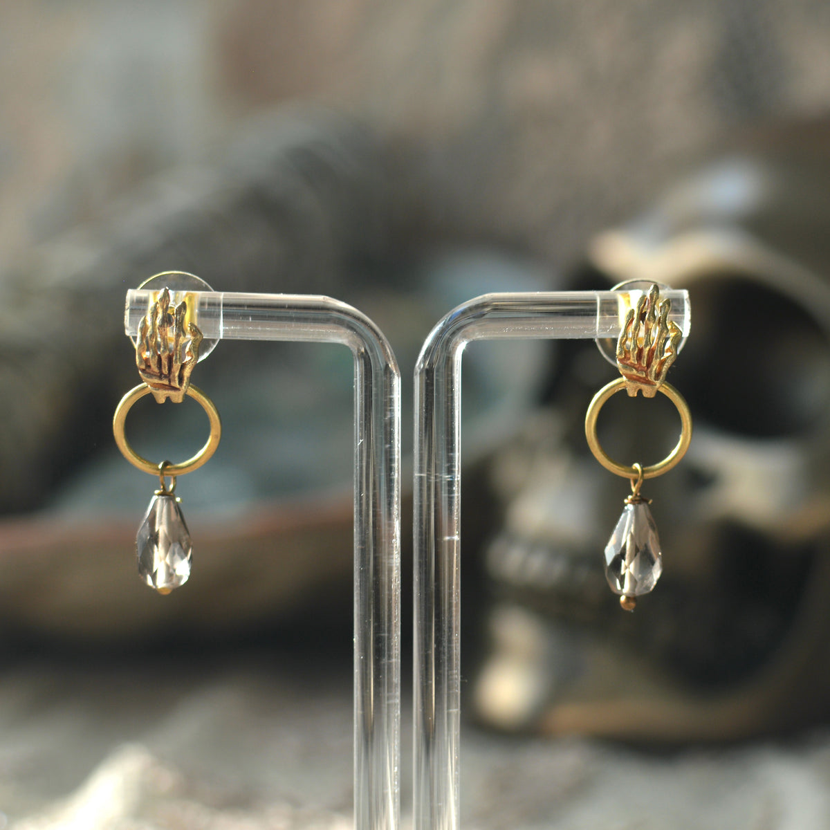 Curved skeleton hands with small hoop and quartz dangle. Displayed on a clear acrylic stand.