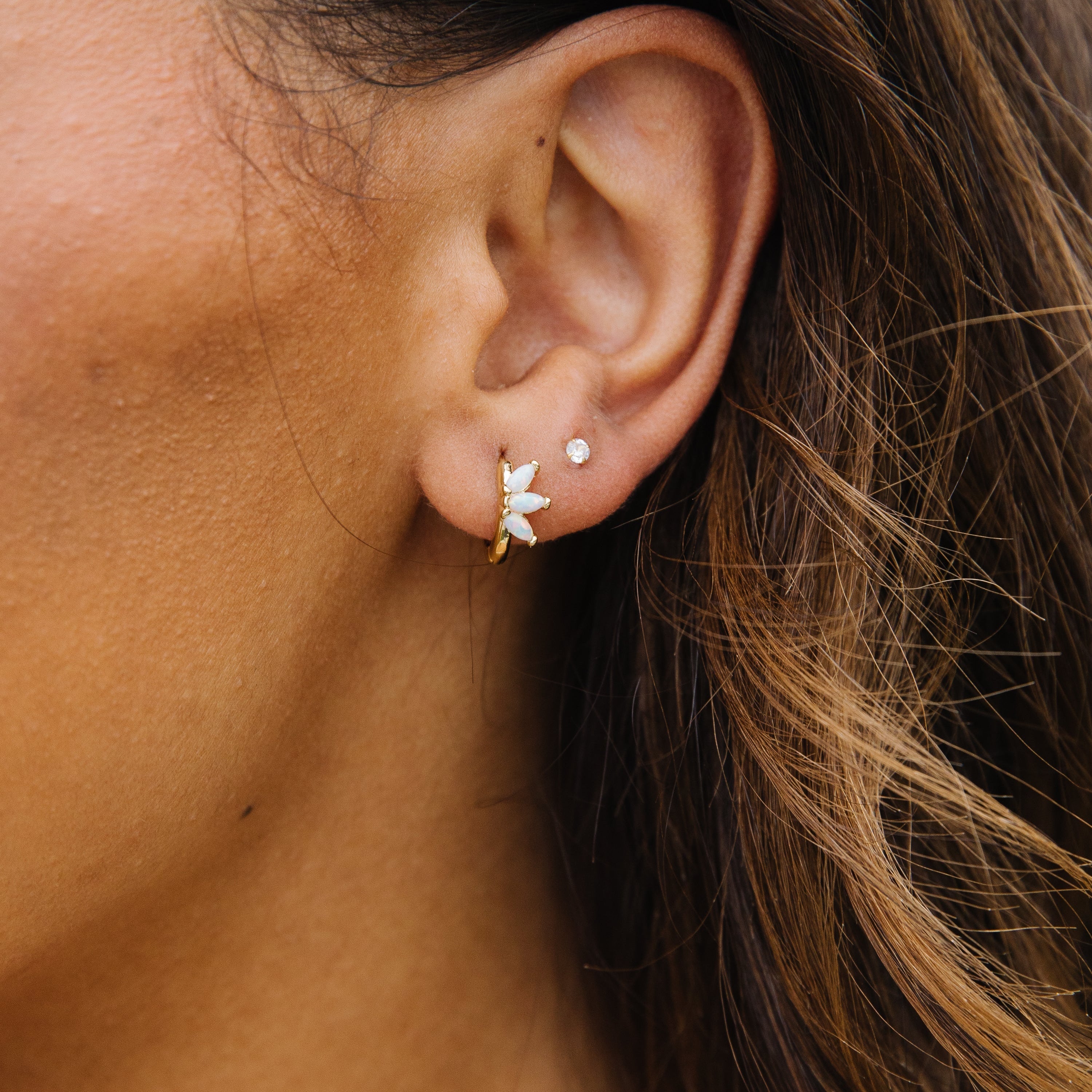 Gold opalite huggie in a woman's ear. 