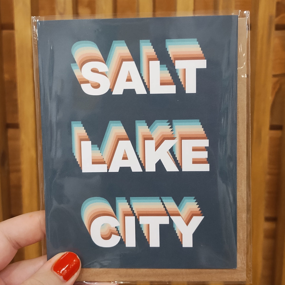 forest green card with funky colorful SLC. pictured in hand against wood backdrop. 