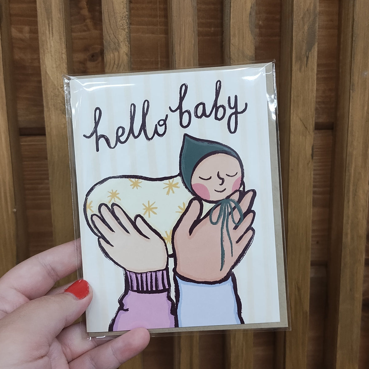 Card with sleeping baby and loving hands illustration, and words "hello baby" written in whimsy cursive along the top. 