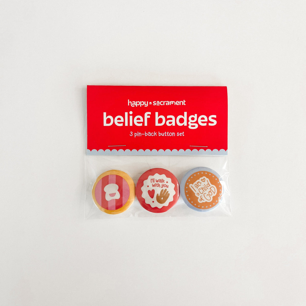 A three-piece “belief badges” pin-back button set is displayed in clear packaging with a red and blue header card. The buttons feature colorful faith-inspired designs, including “I’ll walk with you” and “I’m a child of God.”