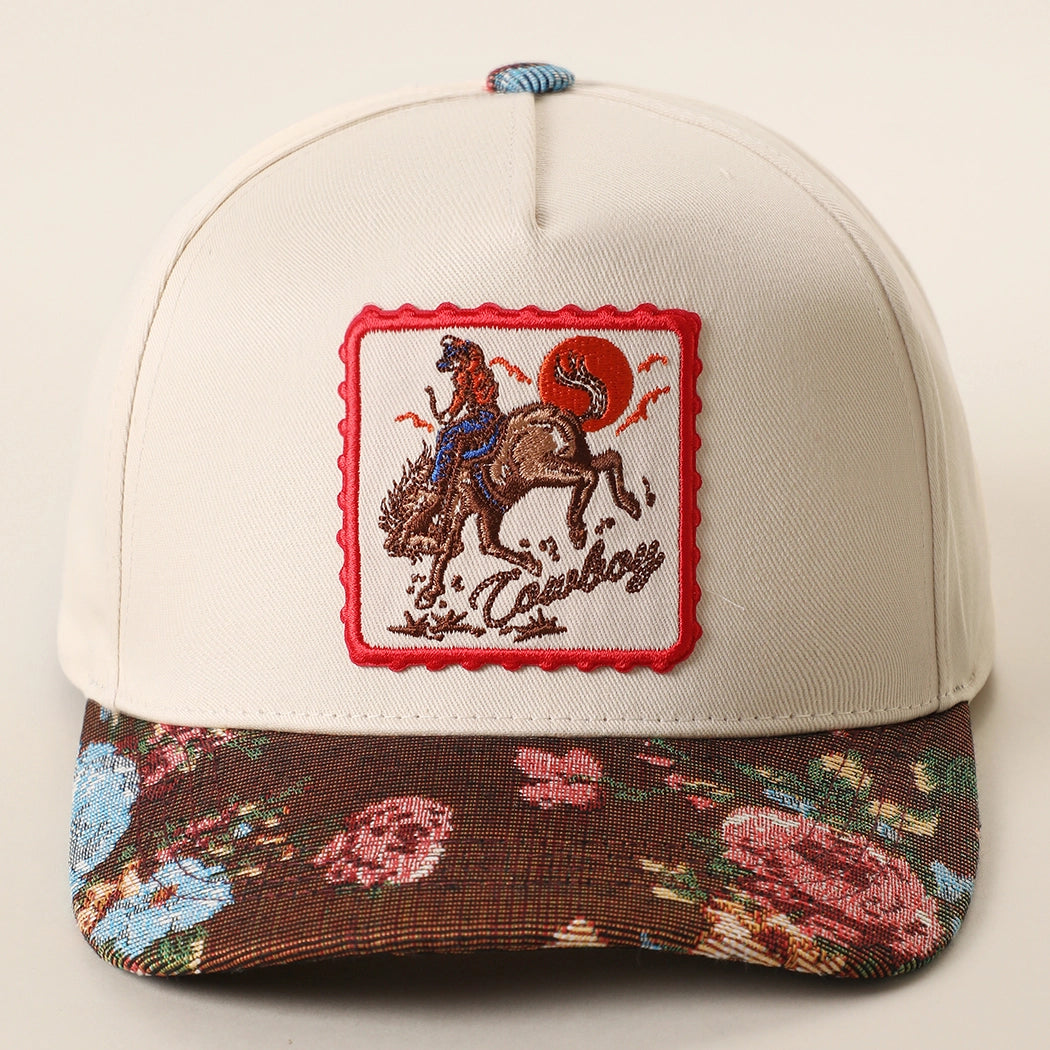 This hat showcases a Western-inspired embroidered patch featuring a cowboy riding a bucking bronco beneath a bold red sun. Detailed stitching, rustic landscape accents, and a scalloped red border create a vintage rodeo look with adventurous country charm and character. Crafted from a 70% cotton and 30% polyester blend, this 5-panel structured baseball cap offers comfortable and durable everyday wear. The floral tapestry pattern brim adds a textured fabric finish.