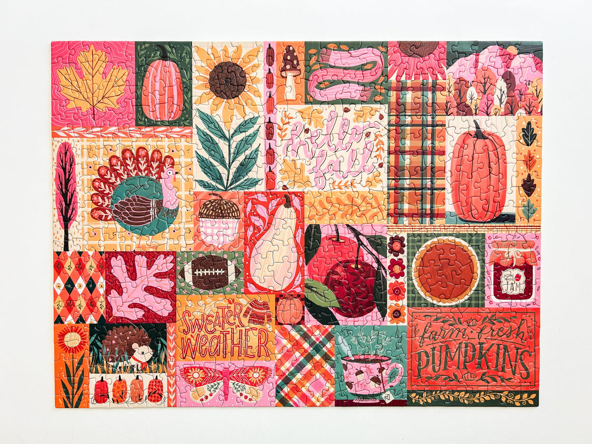 Above view of puzzle. Patchwork style graphics of gourds, plaid, leaves, ect. In reds oranges and pinks. 