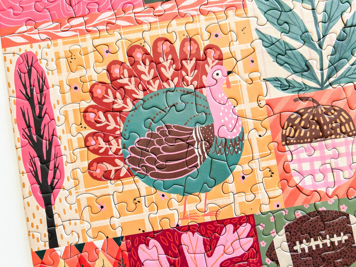 Above view of puzzle. Patchwork style graphics of gourds, plaid, leaves, ect. In reds oranges and pinks. 