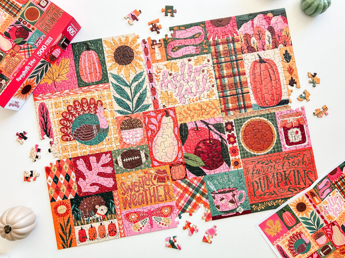 Above view of puzzle. Patchwork style graphics of gourds, plaid, leaves, ect. In reds oranges and pinks. 