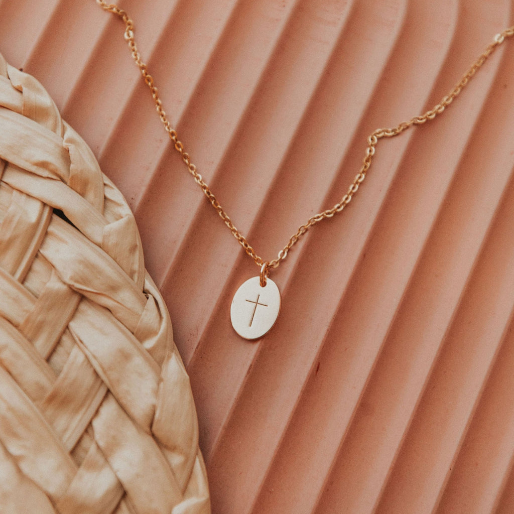 A gold oval pendant engraved with a simple cross, strung on a simple gold chain. 