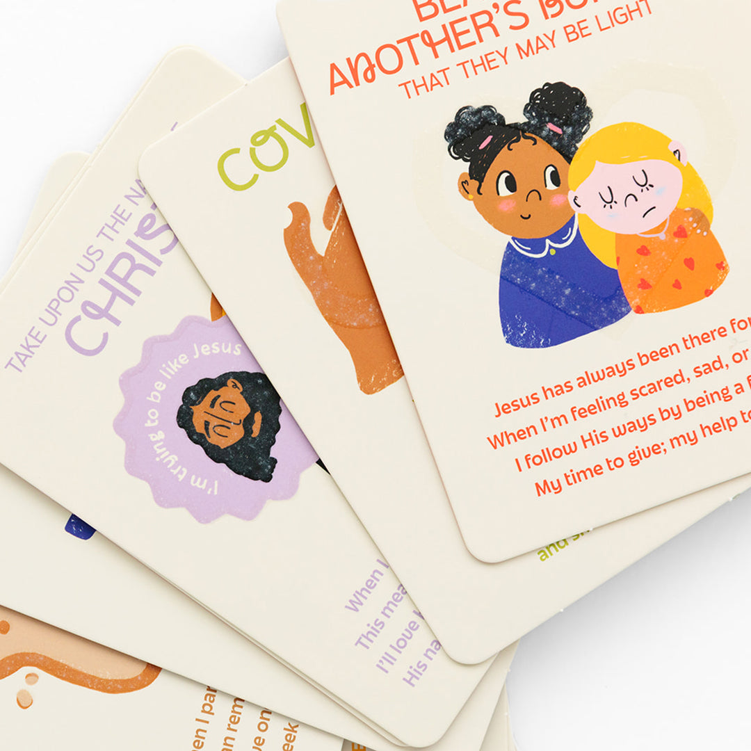 A stack of illustrated devotional cards features colorful artwork of children and Jesus, along with uplifting religious messages in orange, purple, and green text. The cards are arranged overlapping on a white background.