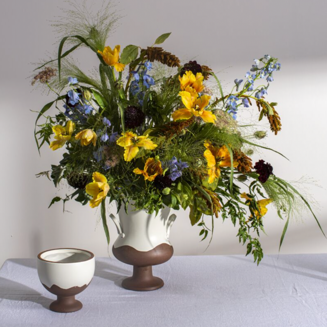Floral arrangement in a decorative vase with two small ceramic items on a white surface.
