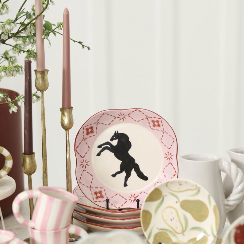 Decorative plates with animal silhouettes on a table setting with candles and mugs.