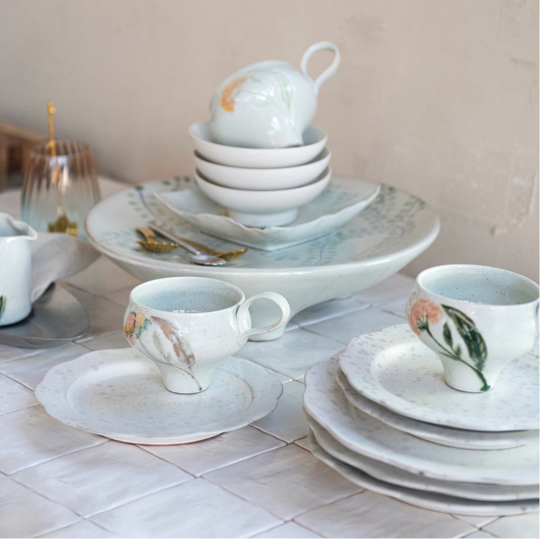 Set of ceramic tableware including cups, saucers, and bowls on a tiled surface.