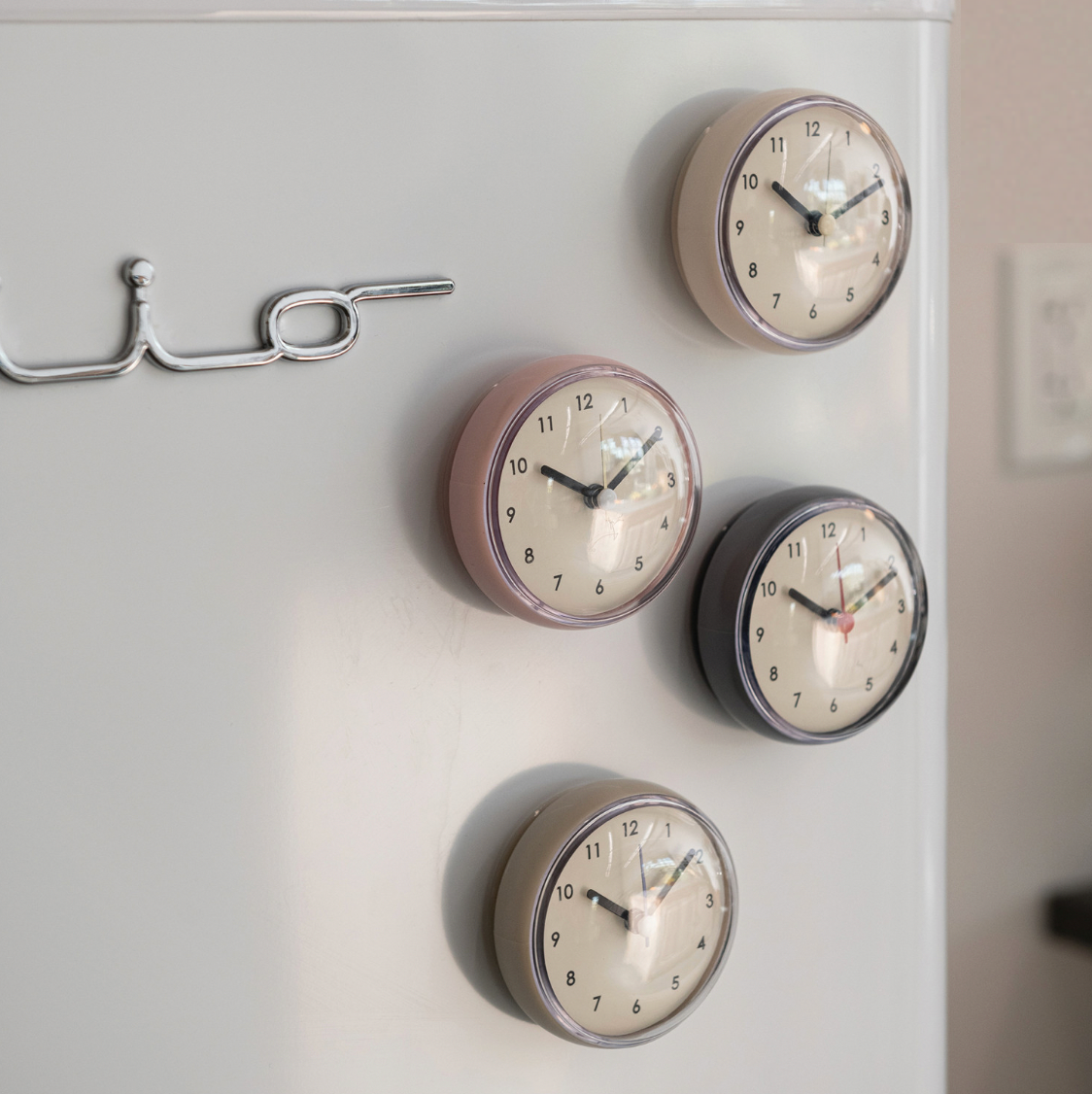 Four round wall clocks of different colors on a white wall.